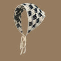 Knitted pet bonnet with black and white checkered pattern and tie strings on brown background