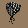 Black and white checkered knit bonnet with ties on brown background, pet apparel accessory