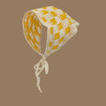 Yellow and white crochet pet bonnet with checkered pattern and tie strings on brown background