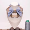 Plaid pet collar with large light blue bow, displayed on mannequin with thread spool nearby.