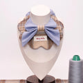 Plaid pet collar with large light blue bow, displayed on mannequin with thread spool nearby.