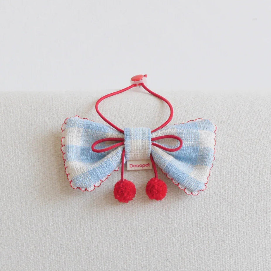 Blue and white plaid pet bow tie collar with red trim and pom poms on a light background